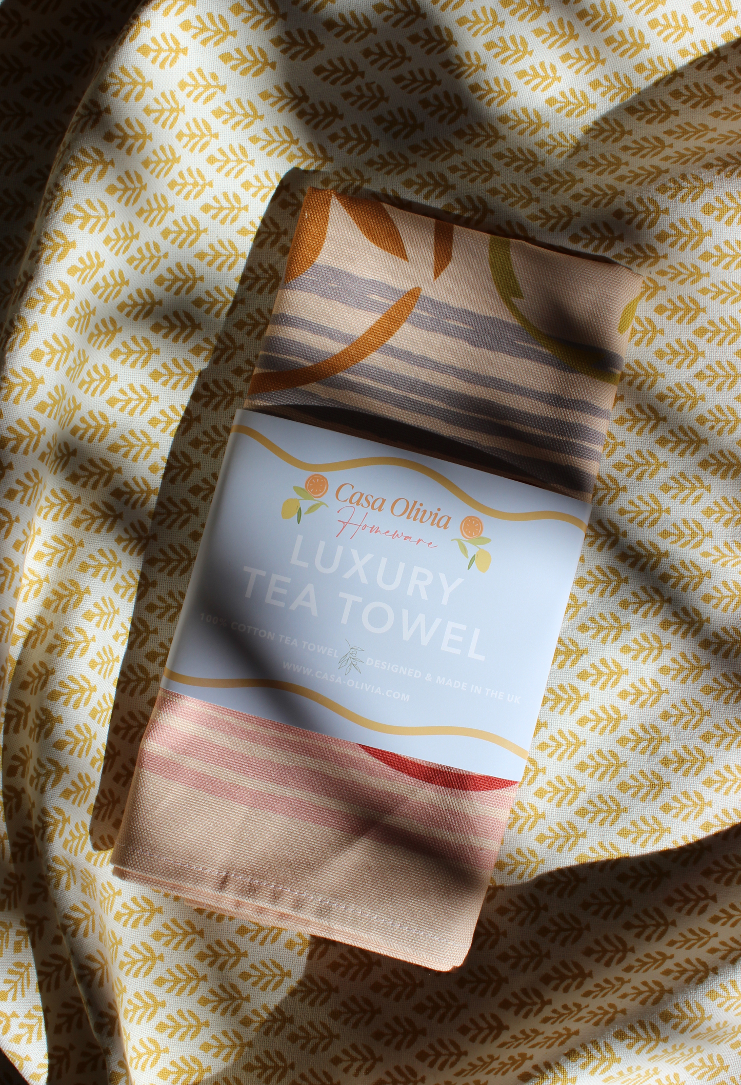 Casa Olivia luxury tea towel on a patterned fabric background