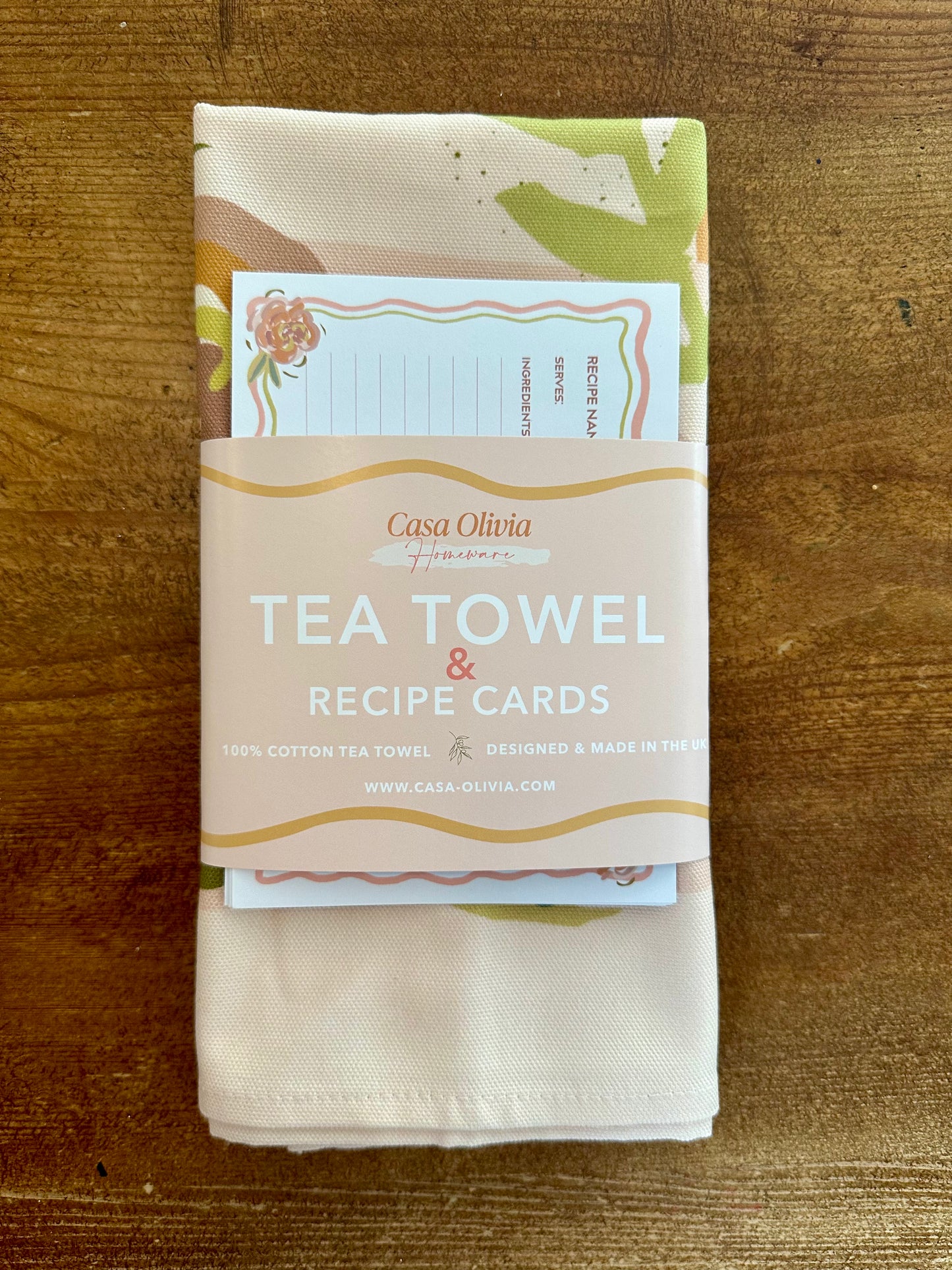 A multicolored floral tea towel with recipe cards wrapped together with a string, placed on a wooden surface.