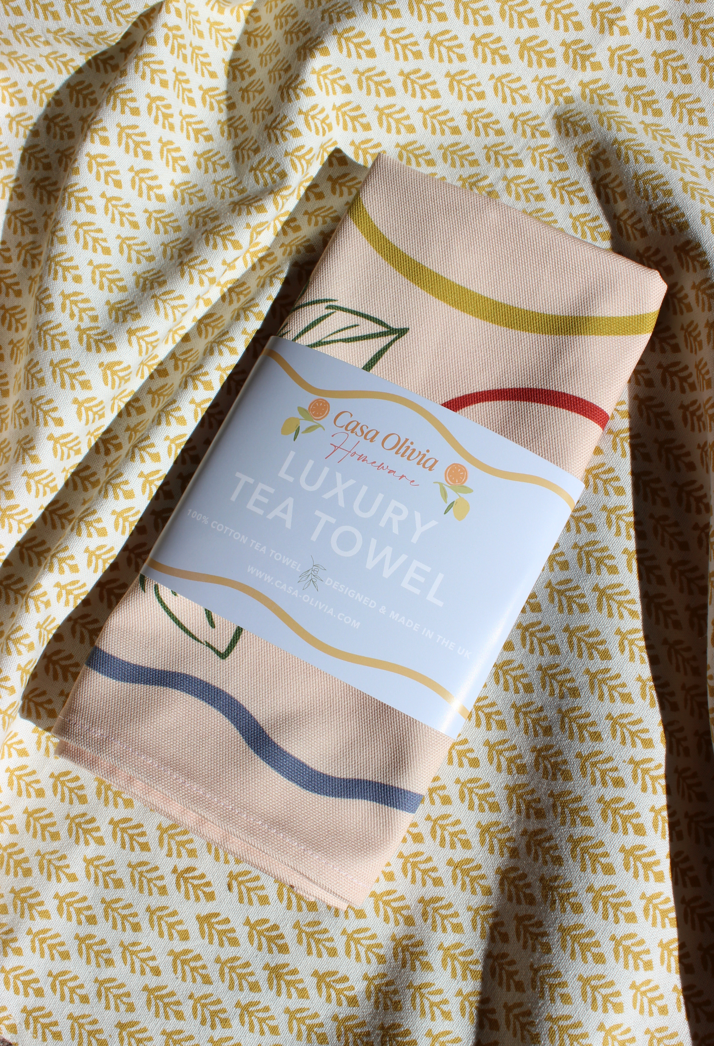 Casa Olivia luxury tea towel with decorative label on a patterned background