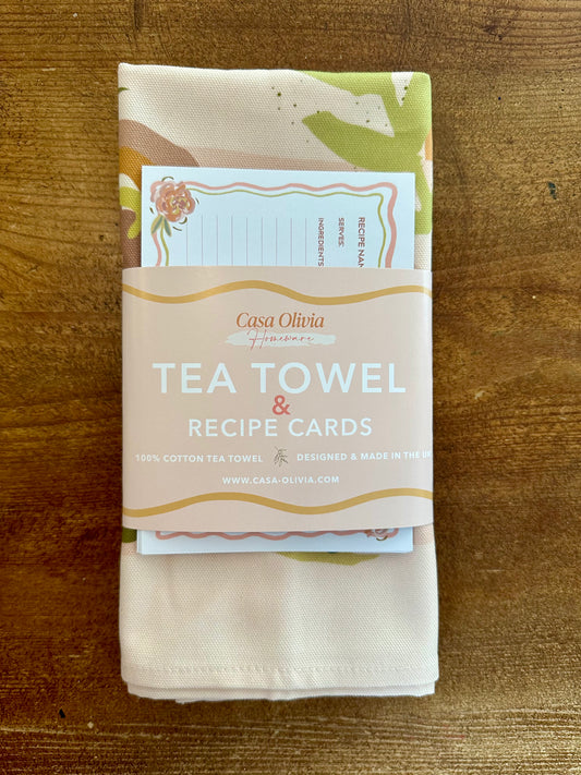 A multicolored floral tea towel with recipe cards wrapped together with a string, placed on a wooden surface.