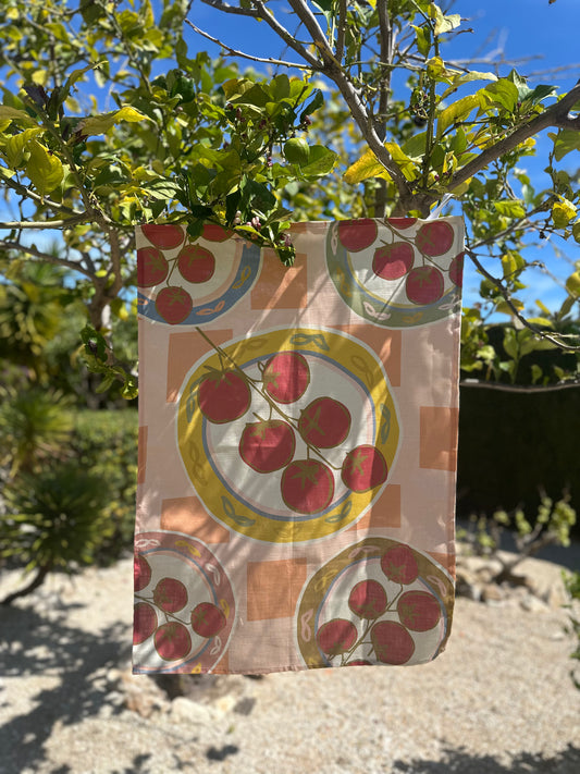 A multicolored tea towel with a hand-drawn tomato design hanging on a loop against a natural background.